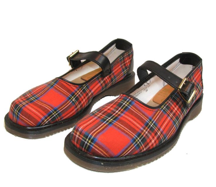the image shows a pair of mary jane shoes with a red and blue tartan plaid pattern. they have black leather straps with gold buckles. the shoes have a black rubber sole. they are placed on a white background.