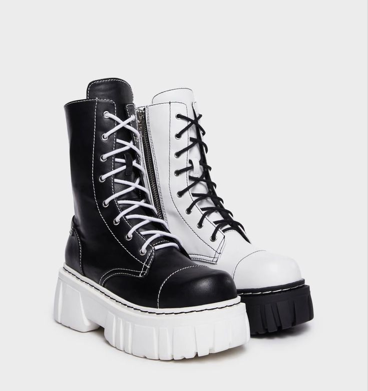 a closeup shot of a pair of black and white platform boots. the boots are laceup with a chunky white sole.  one boot is predominantly black leather with white stitching and a white sole, while the other is predominantly white leather with black stitching and a black sole, creating a yinyang effect.  the boots are positioned slightly angled, showing both the side and the front. the background is plain grey.