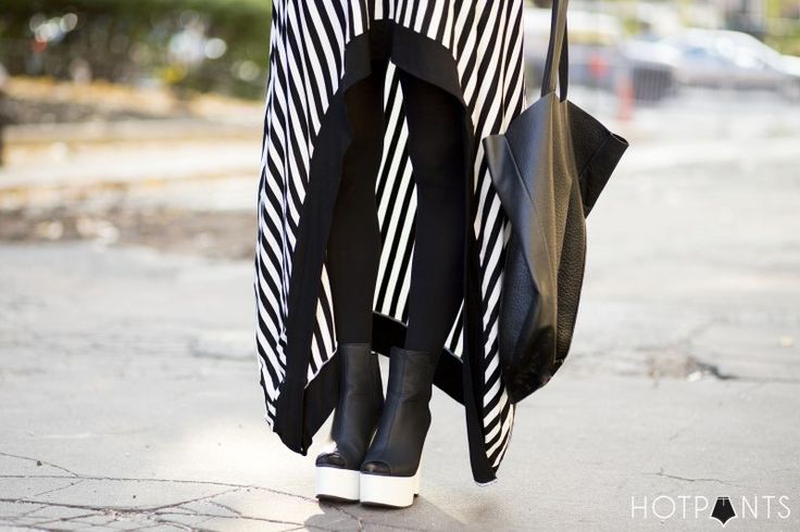 a fashionforward image featuring a person's lower half, showcasing their unique street style. the individual is wearing a striking black and white striped garment, paired with sleek black leggings. they are standing on a concrete surface, complemented by peeptoe heels with a thick white platform. a black leather tote bag is hanging on one side, adding an edgy touch to the ensemble. the image is welllit and conveys a sense of modern fashion.
