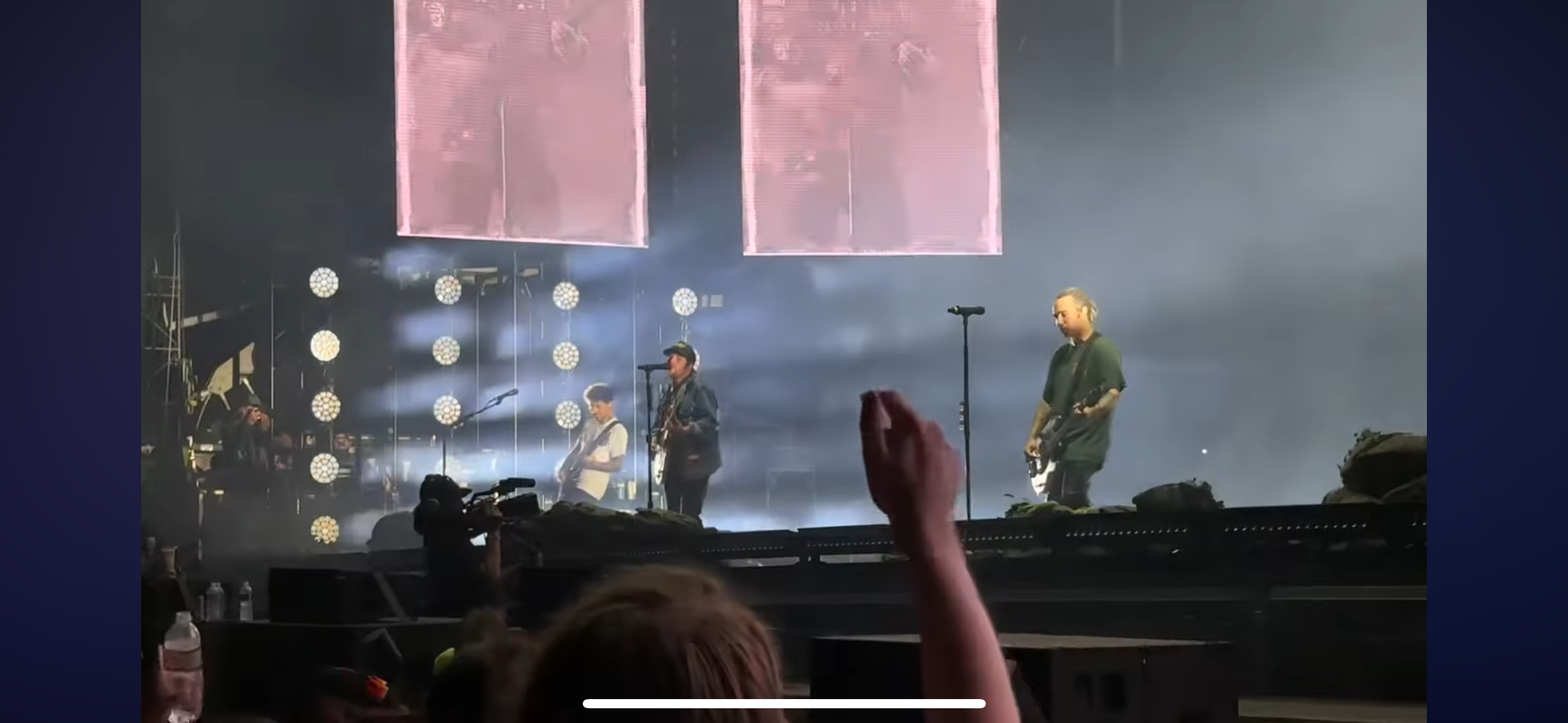 a live concert with a band performing on stage, the band is composed of four musicians, they are playing instruments and singing. there is a crowd in front of the stage, the stage is lit up with bright lights.