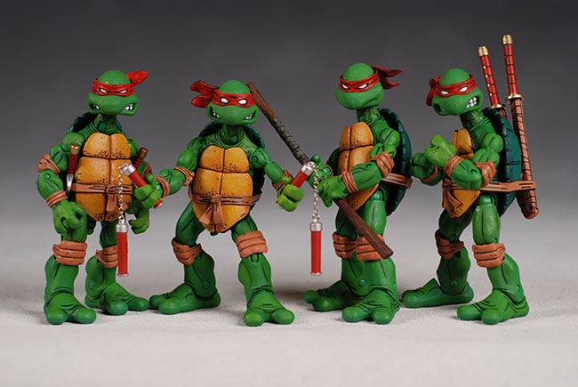 the image shows four teenage mutant ninja turtles action figures standing in a line. each turtle has a red bandana and carries a signature weapon: nunchucks, a bo staff, and katana swords. they have orange shells. they are set against a gray background.