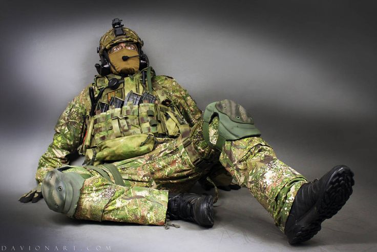 a soldier wearing camouflage gear and helmet,  sitting with his right leg extended and his left leg bent, he is  looking up to the sky with serious expression on his face. he is carrying a lot of equipment. his helmet has a face mask and goggles. his uniform is covered in camouflage patterns. he is carrying a weapon in his holster.