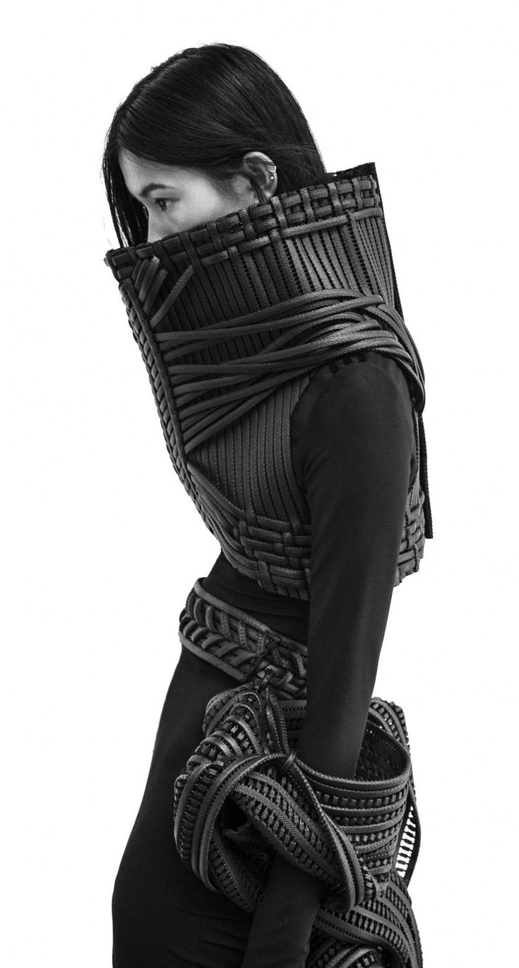 a woman in a black, futuristic, leather outfit poses for a portrait. her hair is pulled back and her expression is serious. the outfit is striking and dramatic, with its intricate, woven details and  edgy, contemporary styling.  she is looking off to the side, suggesting a sense of mystery and intrigue.