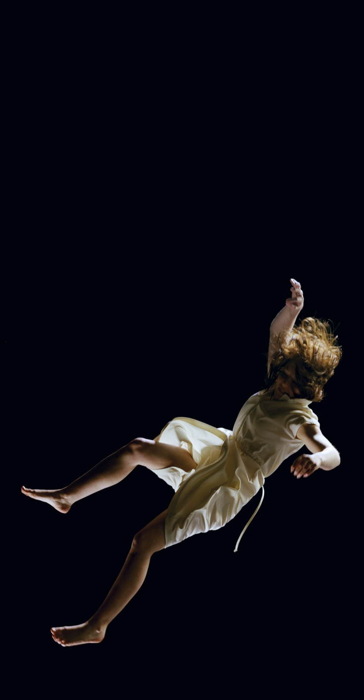 a woman in a white dress is falling through the air, silhouetted against a black background. her arms are outstretched and her legs are bent, as if she is trying to catch herself. the image is dynamic and graceful, capturing the moment of her descent. the dark background emphasizes the movement of the woman and the dramatic lighting creates a sense of suspense.