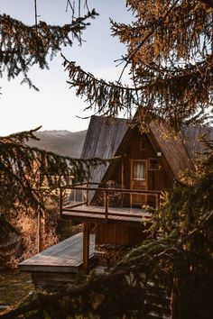 the image showcases a charming aframe cabin nestled amongst lush evergreen trees. the cabin is constructed of wood, exhibiting a rustic aesthetic.  a wooden balcony or deck extends from the front of the cabin, providing an outdoor space. the setting appears to be in a mountainous region, with the suggestion of hills or mountains visible in the distance. the light suggests either early morning or late afternoon/sunset, casting a warm, golden hue over the scene. the overall ambiance is peaceful, inviting, and reminiscent of a cozy retreat in nature.  the trees in the foreground partially obscure the view of the cabin, adding depth and a sense of seclusion.