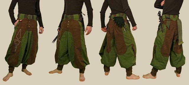 the image showcases a pair of men's  loosefitting, twotoned pants (green and brown) with a unique design aesthetic. they appear to be inspired by medieval or fantasy styles.  the pants feature patchwork detailing, embroidery on one side, and are held up with a wide belt.  the model is shown from the front, back, and side to demonstrate the cut and fit of the pants. the pants have a harem style that is baggy at the top and tapers slightly to the ankle, which is where they finish with a cuff.  the overall style appears handmade or artisancrafted.