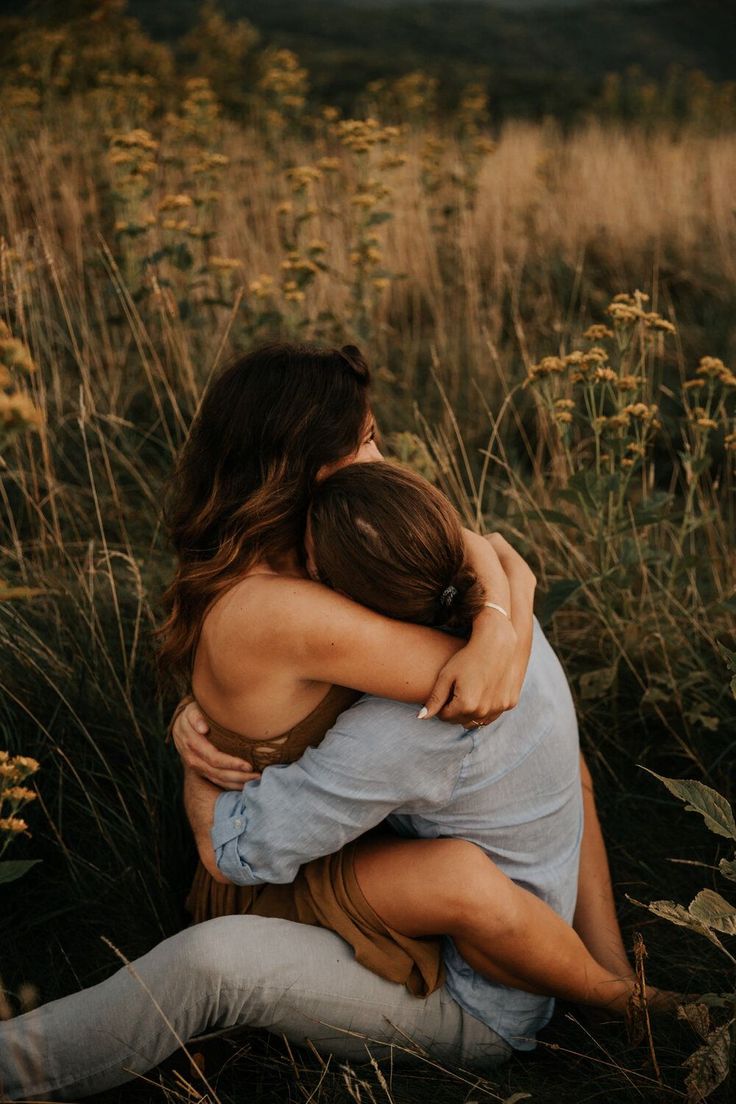 a couple is hugging each other in a field of tall grass, embracing in