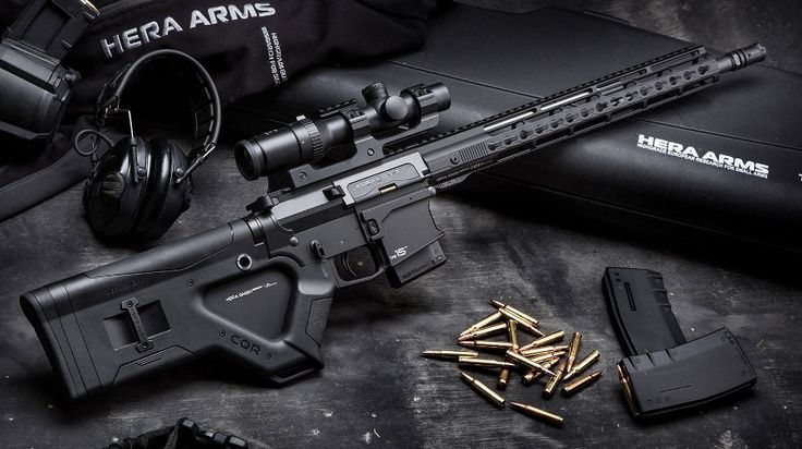 the image shows a black hera arms ar15 rifle with a scope, magazine, and ammunition displayed on a black surface, along with headphones and a bag, showcasing the rifle and its accessories.