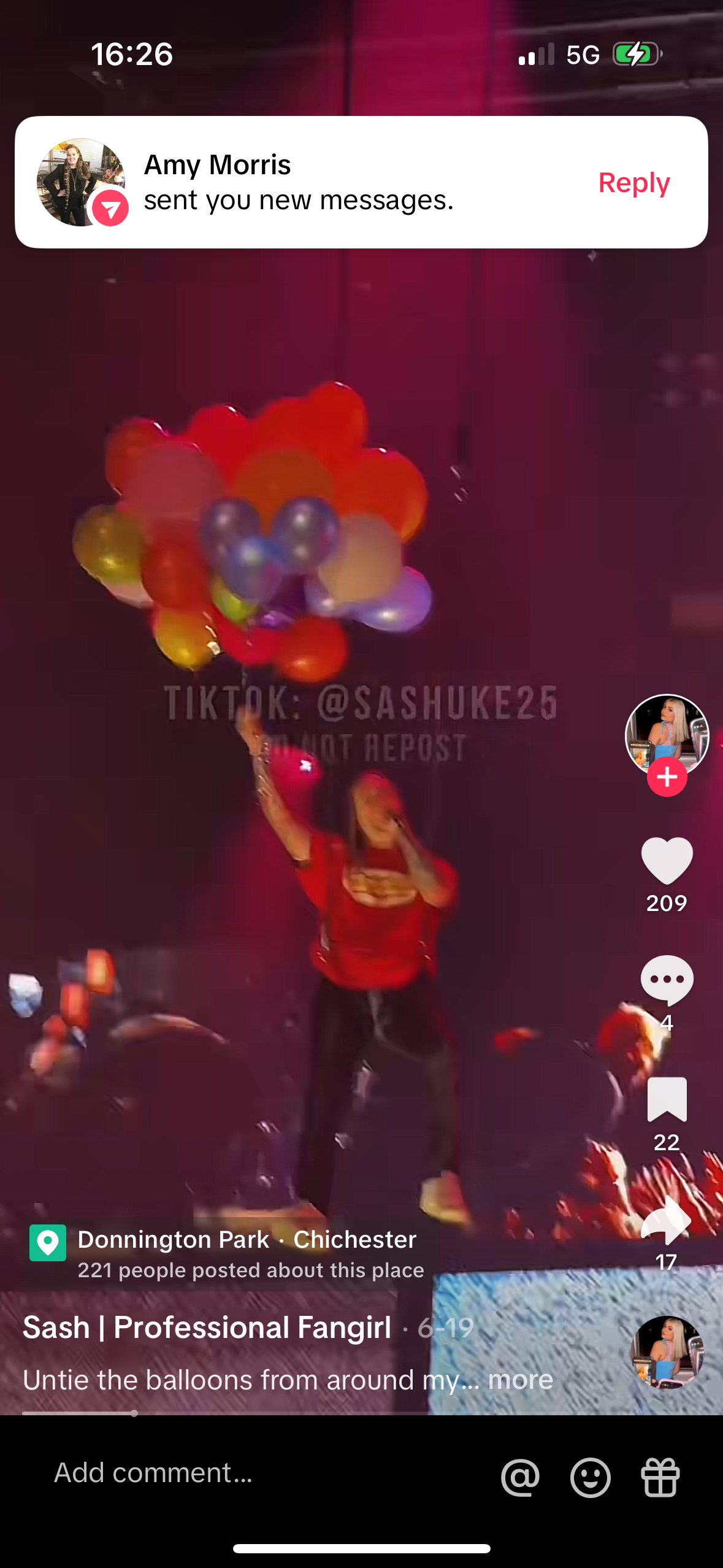 a screen capture of a tiktok video. the video is of a woman in a red shirt and black pants holding a bunch of balloons. she is looking at the camera and the caption of the video says "untie the balloons from around my...". the tiktok handle is @sashuke25. it shows the number of likes, comments and shares. there are also details of the location of the video which is donnington park, chichester. in the top left corner, there is a message notification from "amy morris".