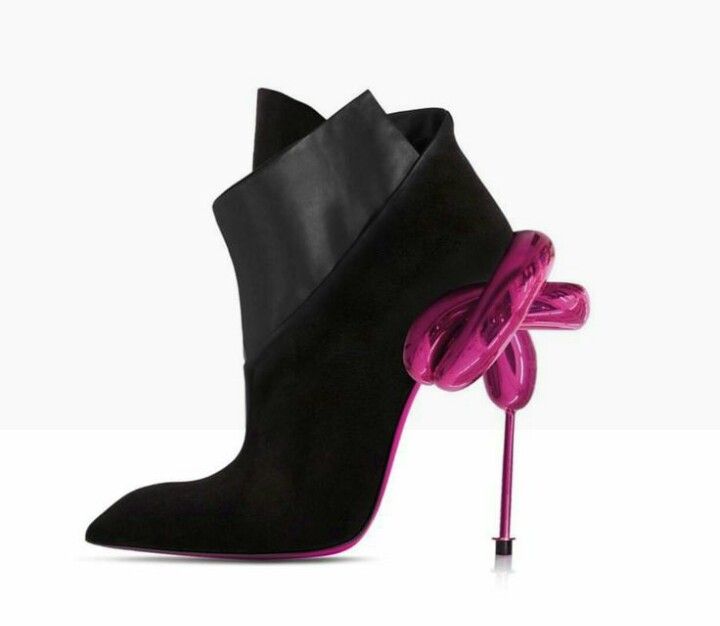 a single black suede ankle boot with a high stiletto heel stands on a white surface. the boot has a pointed toe and a foldedover collar featuring a band of smooth black leather. the striking heel is a glossy pink sculpture of a balloon dog, appearing as if the dog is supporting the back of the shoe. the bottom of the shoe is also lined in pink.
