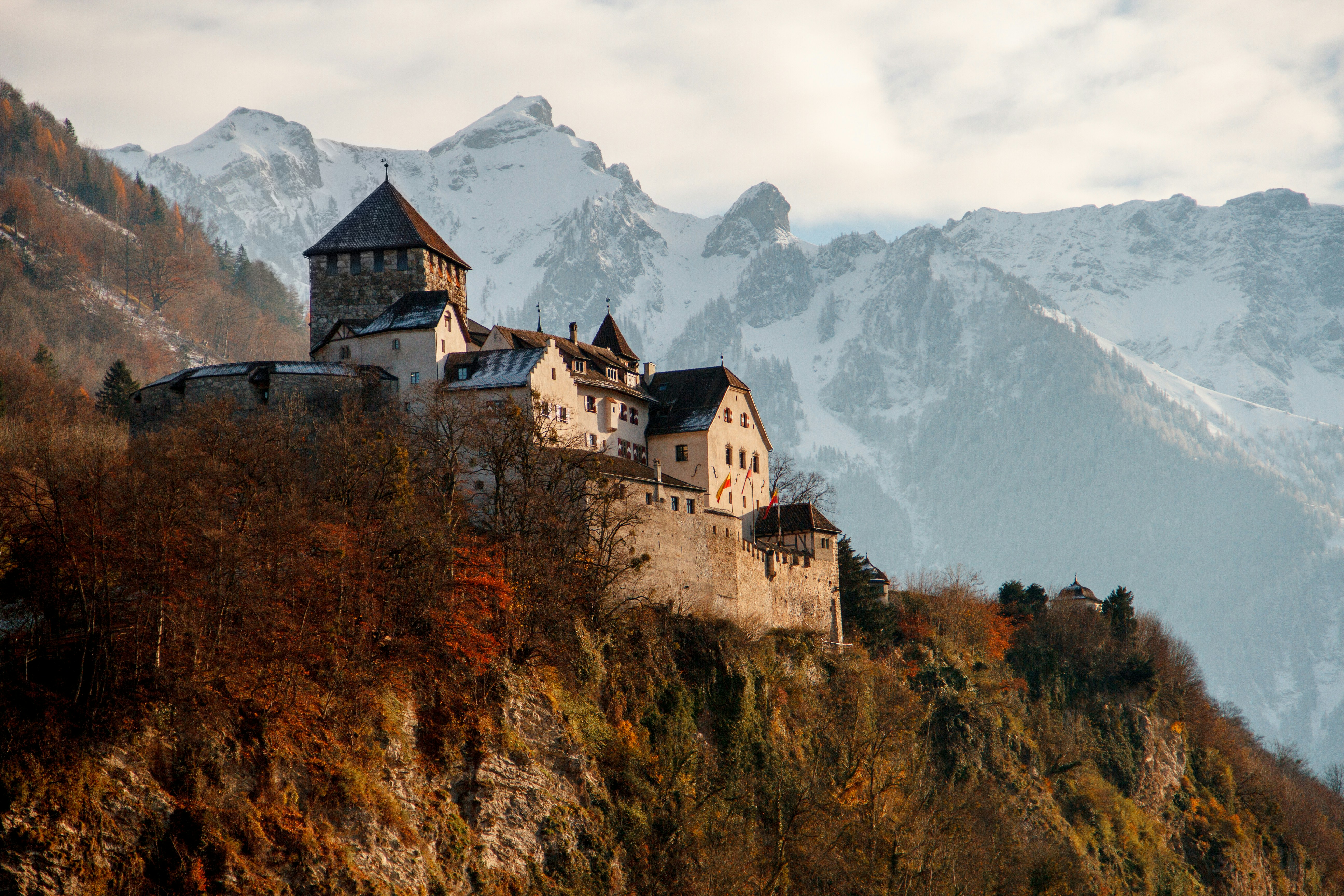 a castle sits atop a snowcovered mountain, surrounded by a lush forest. the castle is a beautiful example of medieval architecture, with its stone walls and pointed towers. the mountains in the background are covered in snow, and the sky is a clear blue. the scene is both majestic and peaceful.