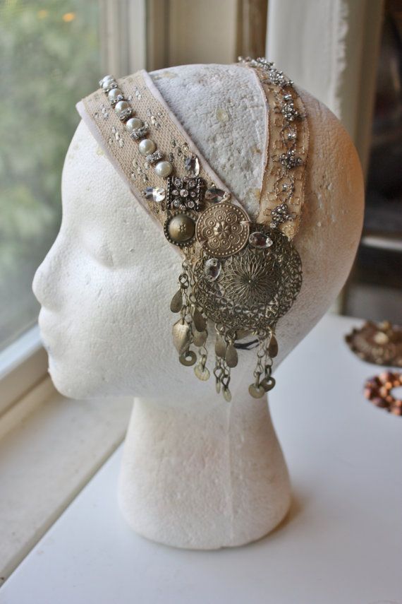 this is a white headband with silver and gold jewelry attached to it. the headband is adorned with small beads and other decorative elements. it is worn on a white mannequin head.