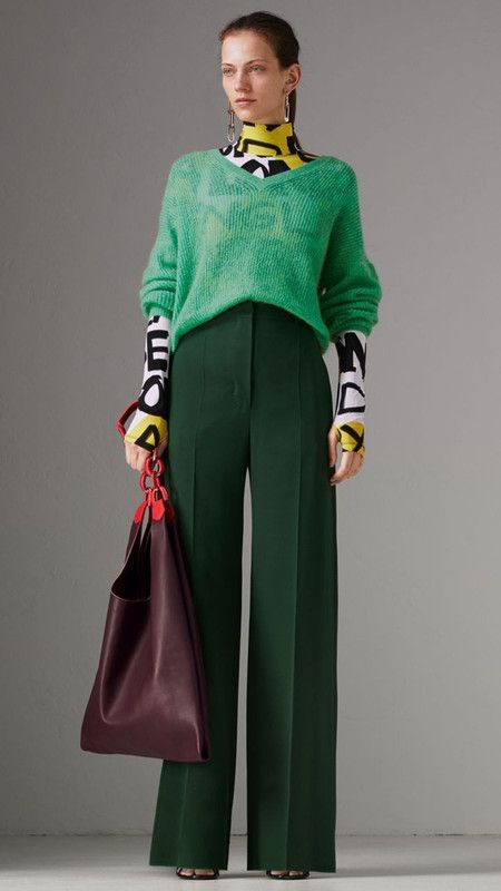 a woman is posing in a green sweater and pants with a burgundy bag, looking fashionable and chic. she is standing with one hand on her hip and the other holding the bag's strap. her long, dark hair cascades down her shoulders, framing her face. the overall composition is stylish and captures the woman's sense of fashion.
