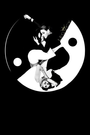 two women are shown in a yin yang symbol in a contemporary dance performance. they are wearing black and white clothing. the woman on top of the other woman is upside down. both women are flexible. the women are performing the dance in a circle with a black and white background.