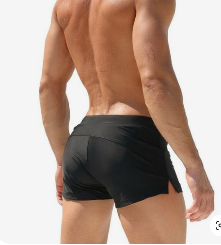 the image showcases a muscular man from the back, wearing black swim trunks. he is standing on a beach under natural sunlight. the focus is on the fit and style of the swim trunks.