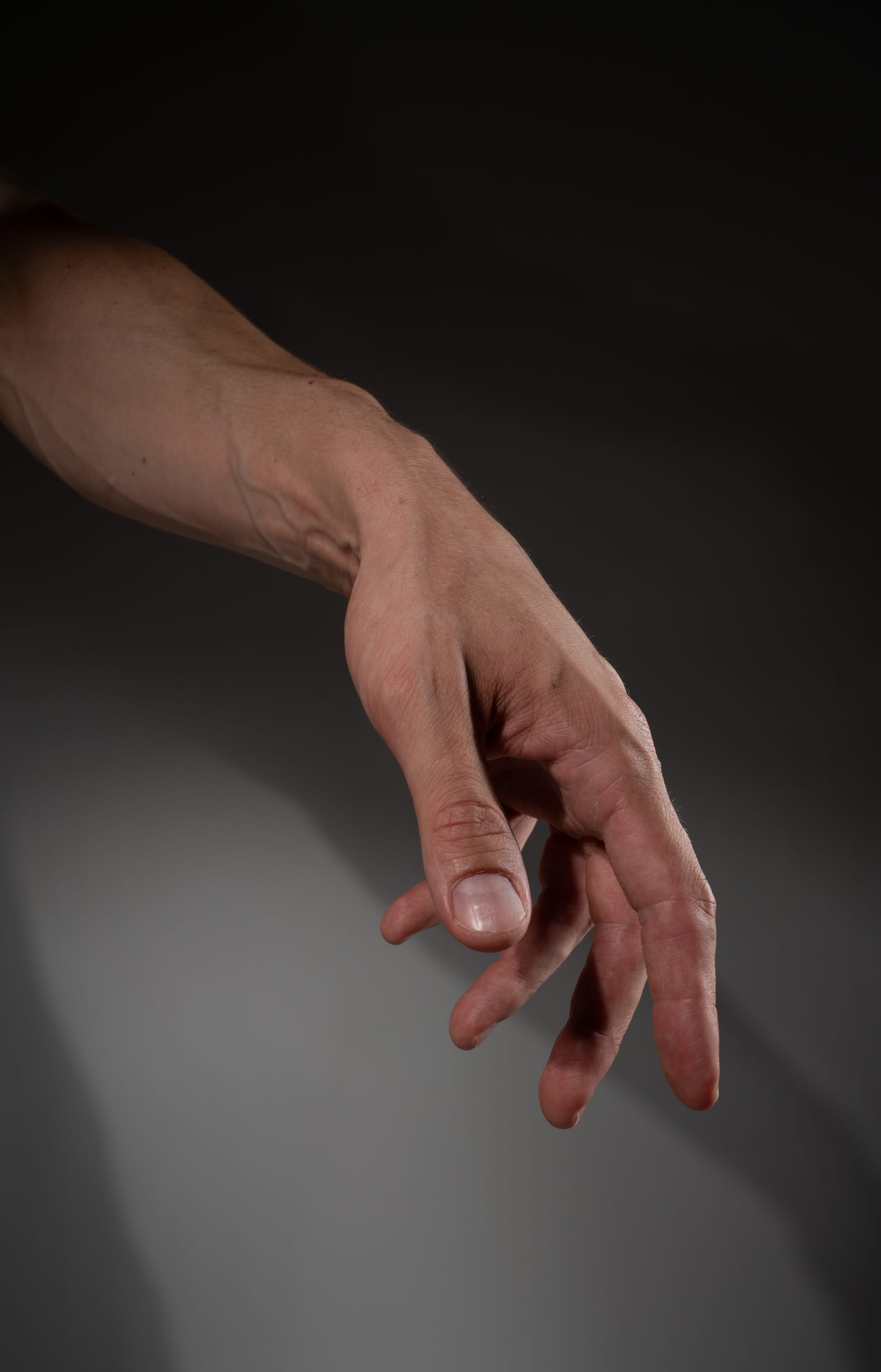 a caucasian male's right arm extended out with fingers slightly curled, as if reaching for something. the arm is lit with studio lighting highlighting the subtle contours and details of the hand and arm.