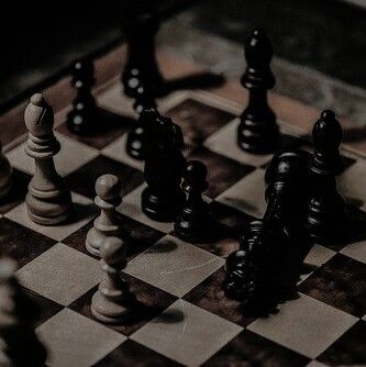 a closeup shot of a chessboard with black and white chess pieces arranged on the board. the chessboard is made of wood and the pieces are made of darkcolored material. the background is dark and shadowy, creating a dramatic and mysterious atmosphere. the image is a representation of the game of chess and its strategy and competition.