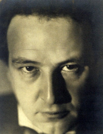 the image is a closeup black and white portrait of a man.  the photograph is taken from a slightly low angle, emphasizing his strong facial features.  the man's expression is serious, almost pensive, with a thoughtful look in his eyes.  the lighting is dramatic, utilizing strong shadows to accentuate the contours of his face and create a moody atmosphere. his hair is dark and appears somewhat slicked back. the overall style suggests the photograph is from the 1920s or 1930s, with a classic, artistic feel. the high contrast and use of shadow contribute to a powerful and evocative portrait.