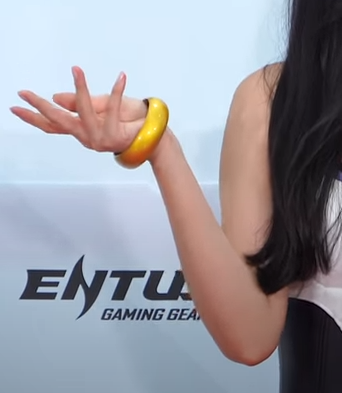 a closeup image showcasing a woman's arm adorned with a vibrant yellow bracelet. the woman is positioned against a backdrop featuring the text "entur gaming gear." her hand is partially raised, with her fingers gracefully extended.