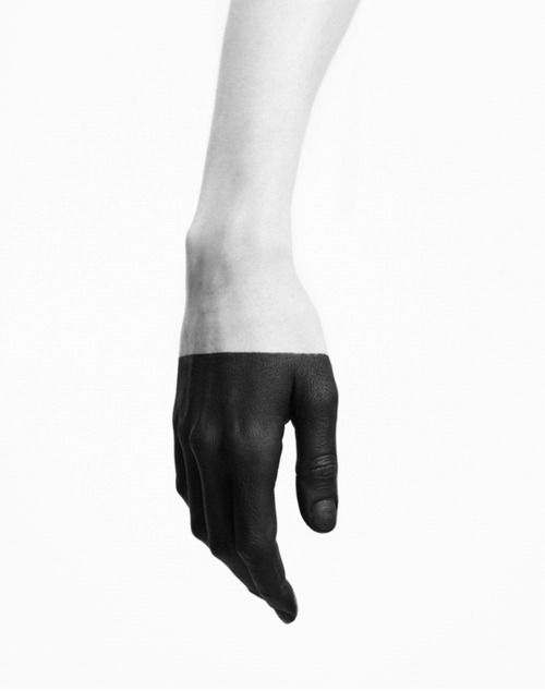 a close up of a person's hand with black paint on the lower half and the upper half of their arm is natural skin color. the arm is slightly raised with the hand relaxed in front of the arm. the background is white, and the image is in black and white.