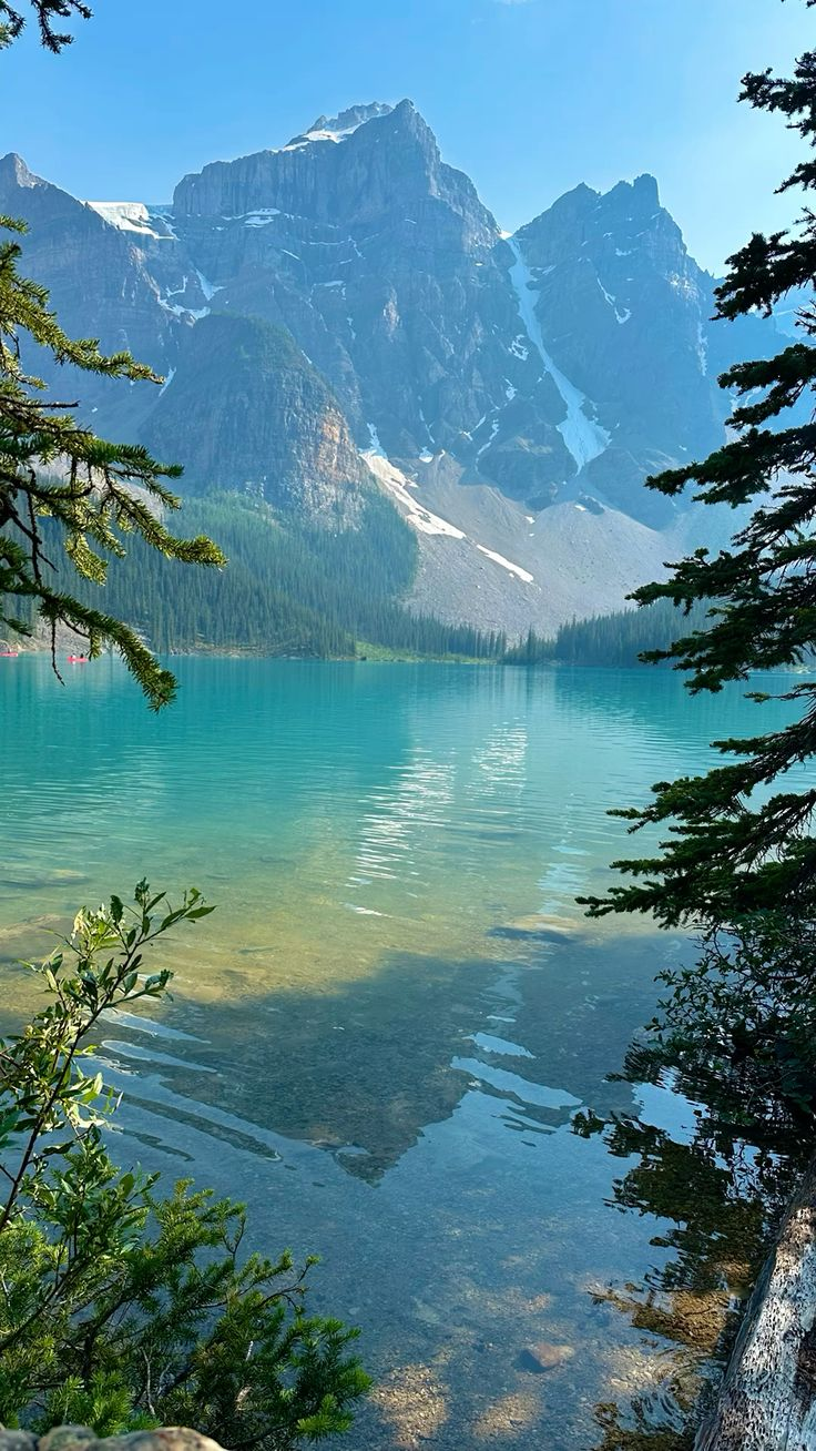 this is a scenic shot of moraine lake, with turquoise water, framed by trees in the foreground. in the background, there are majestic mountains, some with visible snow and glacier remnants. the landscape shows a lush forest on the slopes leading up to the rocky mountain peaks. the water reflects the surroundings, adding depth and beauty to the scene.