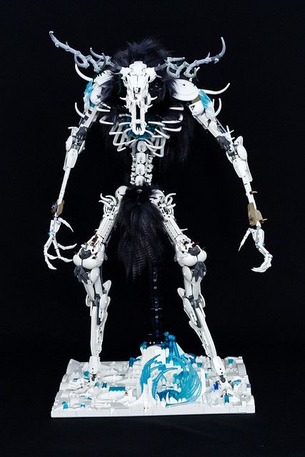 a detailed closeup shot of a meticulously crafted lego model depicting a fantastical creature. the creature is predominantly white and teal, with a skeletal structure and deerlike antlers.  it has a dark, furry mane and tail. the model stands on a white base with a stylized blue water feature.  the lighting and background are dark, making the model the clear focus of the image.  the image suggests a high level of skill and creativity in the lego building process.