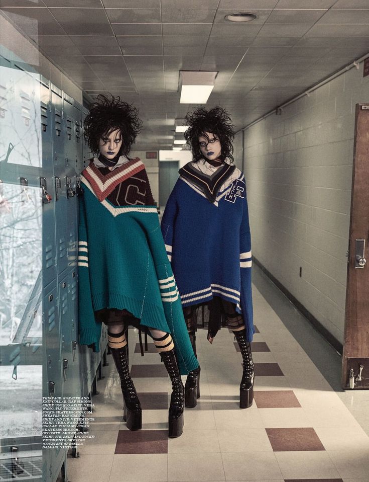 two models dressed in dark, gothic style clothing are posing in a school hallway. one is wearing a green and white sweater with black boots, while the other is wearing a blue and white sweater with black boots. both have long black hair and dark makeup. the hallway is lined with lockers.