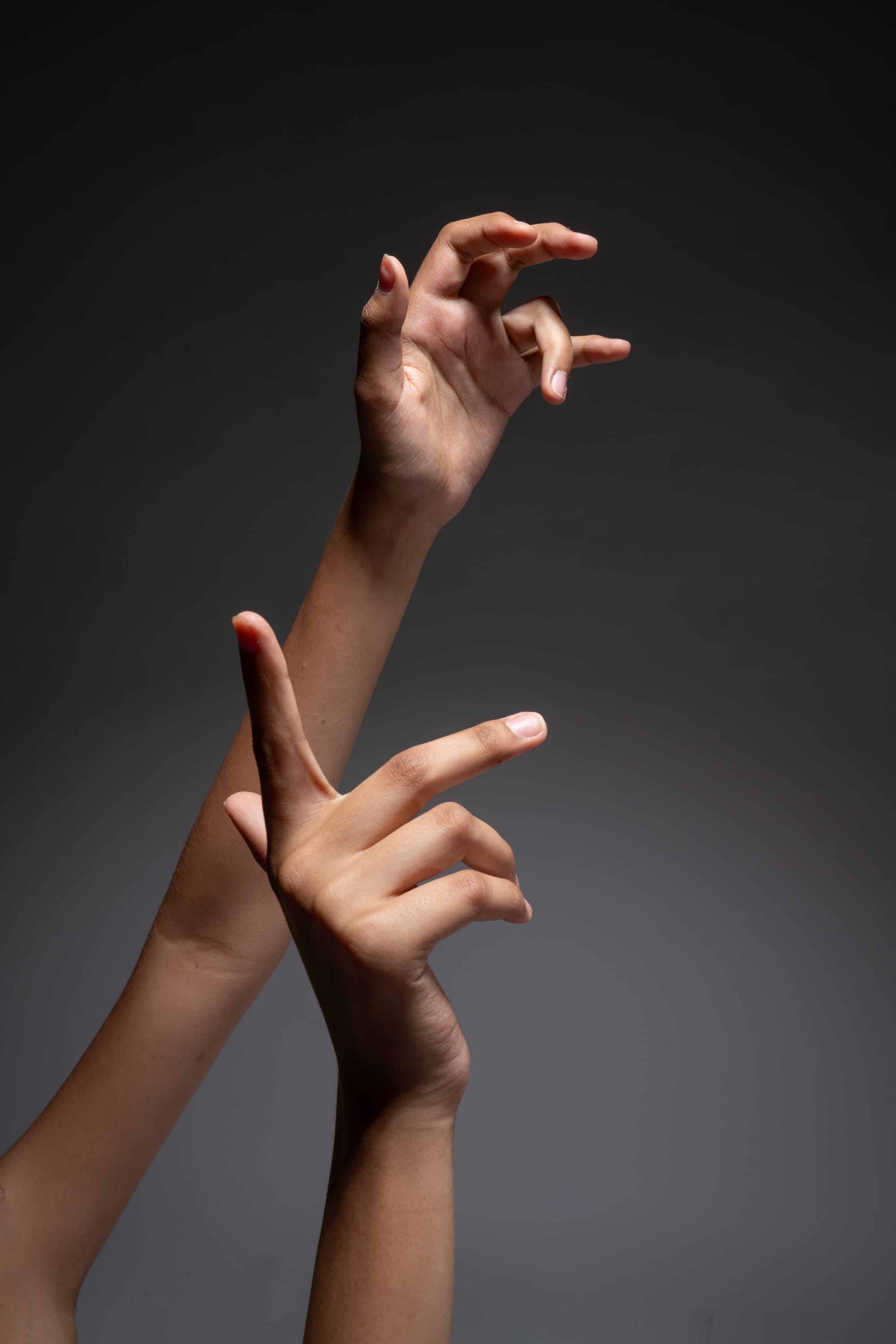 the image features a pair of female hands gracefully posed against a dark gray background.  the hands are illuminated by a spotlight, creating dramatic shadows and highlighting the delicate details of the fingers and skin. the closeup perspective emphasizes the elegance and expressiveness of the hand gestures.