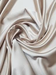 the image shows a swathe of beige silk or satin fabric with a soft, lustrous sheen. it is draped and folded in a way that creates soft waves and highlights the luxurious texture of the material.