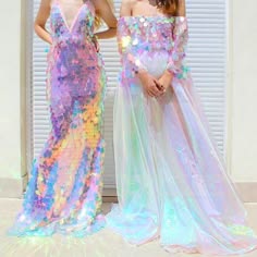 two women are standing side by side in their iridescent dresses, looking very happy and elegant. they are both wearing sequins and tulle, giving them a very mermaidlike look. the first woman is wearing a sequined mermaid dress with a high neckline and a train. the second woman is wearing a tulle dress with sequins in a strapless style and a matching cape. the dresses have a rainbow of iridescent colors that sparkle and shimmer in the light. they look stunning in these outfits!