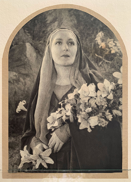 the image shows a black and white, possibly sepiatoned, portrait of a woman dressed as a nun. she is wearing a dark robe and a white veil that frames her face. she holds a large bouquet of lilies and other flowers. the background is blurred but appears to be a garden setting. the portrait is framed in an arch shape, giving it a vintage or antique feel. the overall style is artistic and evocative, possibly inspired by religious iconography. the woman's expression is serene and contemplative. the image has a slightly grainy texture and high contrast, adding to its dramatic effect.