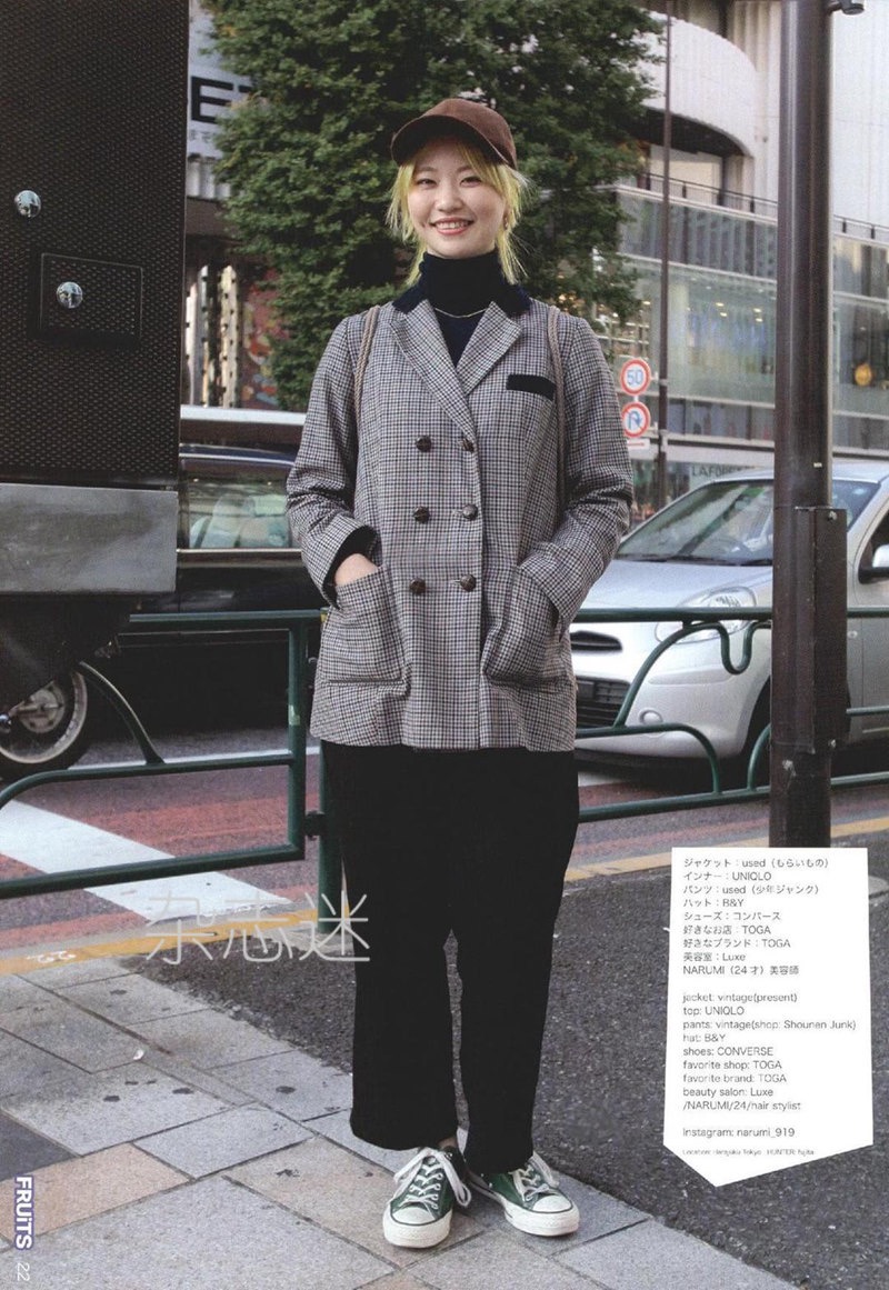 a young woman is standing on a city street, posing for a fashion magazine. she is wearing a gray plaid doublebreasted jacket, a black turtleneck sweater, black wideleg pants, and green converse sneakers. she has short blonde hair and is wearing a brown baseball cap. there is japanese text on the right side of the image, providing information about the woman's outfit and the magazine. the background of the image shows a busy city street with cars and buildings.