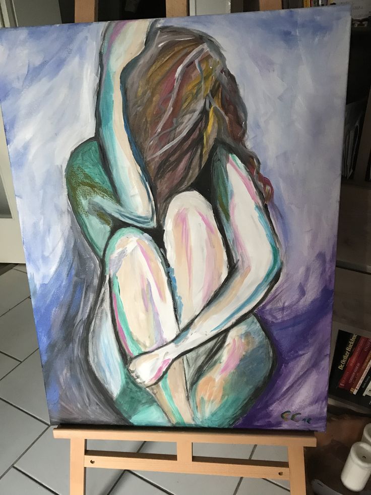 an abstract, colorful painting on canvas depicting a woman sitting curled up with her arms around her legs. the woman is nude and her body is painted in shades of pink, white, green, blue, and yellow. her hair is brown and is painted in a similar style as the rest of the painting. the background is a purple and blue color. the painting is sitting on an easel.