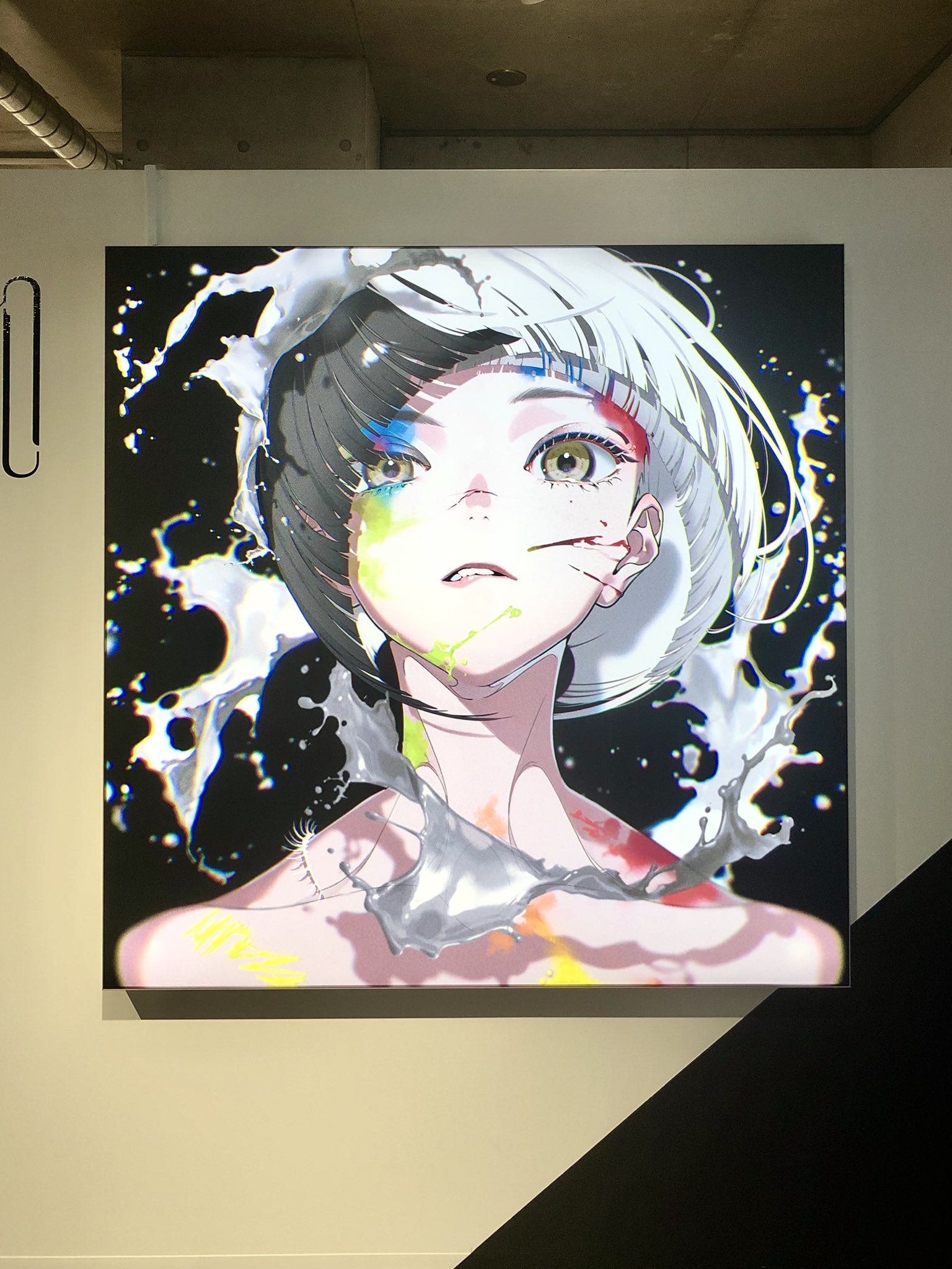 the image showcases a digital illustration of a young woman with a striking, splitcolored hairdo (black and white) and heterochromia, displayed as a lightbox art piece in a gallery setting. the artwork features a glitch art aesthetic, with digital noise and color distortions. the woman's face and upper body are splattered with vibrant paint, resembling a dynamic action shot. the background is predominantly black, contrasting sharply with the white paint splashes that frame her figure. the lighting appears to be artificial, possibly from a spotlight, highlighting the artwork against the clean, minimalist gallery wall.