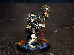 a miniature of a space marine librarian from the warhammer 40,000 tabletop game, painted in grey and blue, stands on a base decorated with a fiery effect. the librarian is armed with a force staff and wears ornate power armor.