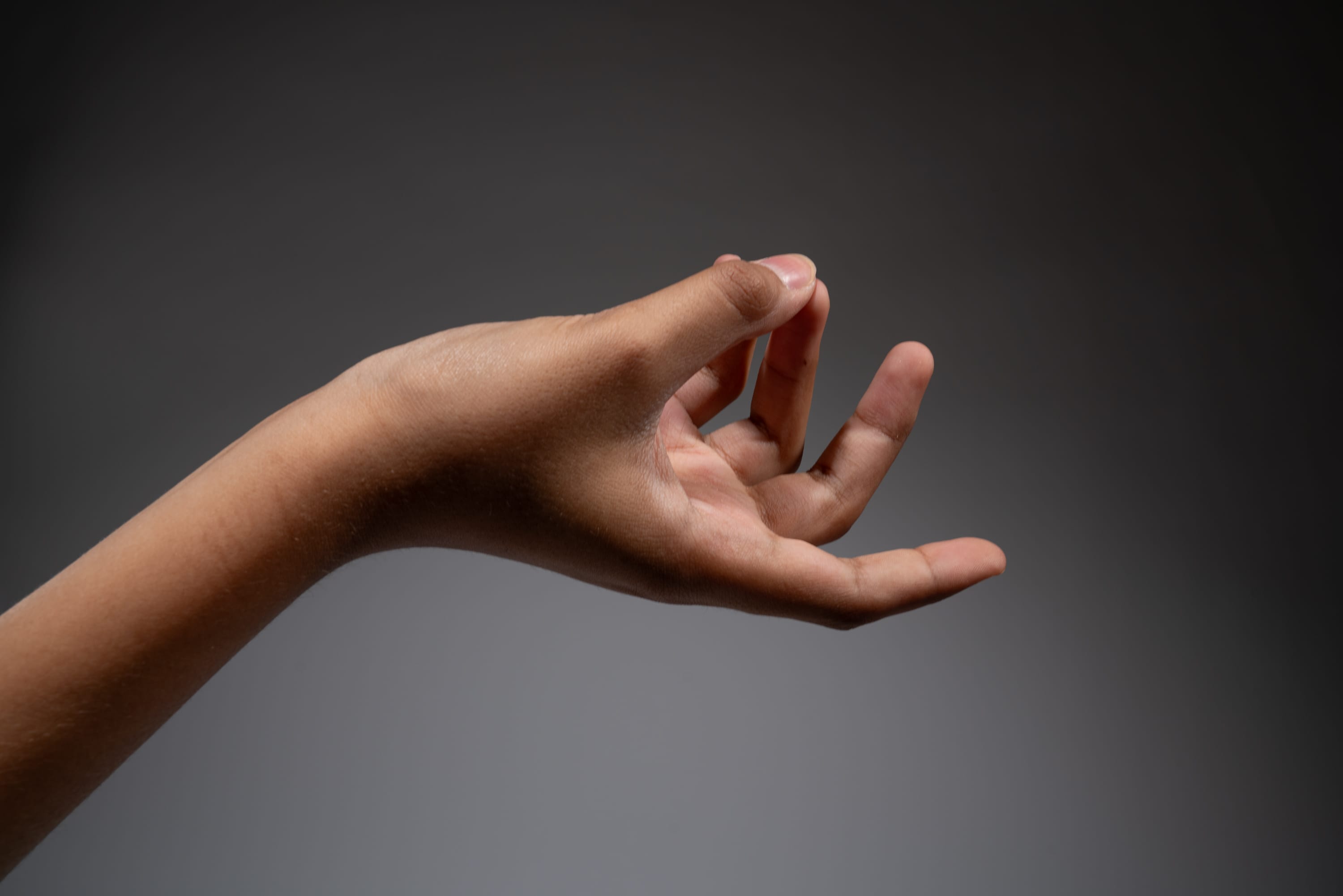 a hand is reaching out with thumb and forefinger touching. the background is gray.