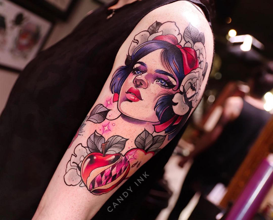 the image shows a freshly done neo traditional tattoo on someone's upper arm. the tattoo is a portrait of snow white with white flowers, a red bow, and a poisoned apple with a bite taken out of it. the tattoo is done in a illustrative style with bold lines and vibrant colors. the background of the image is the tattoo parlor where the tattoo was done.
