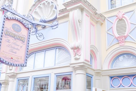 a pastelcolored storefront with an ornate sign that reads "confectionery." the building is decorated with pastel pink, blue, and white colors and features detailed architectural elements like a large scallop shell, a starburst design above the windows, and an octagonshaped archway. the storefront's windows are adorned with delicate blue trim and the sign is an elaborate, decorative piece. the overall effect is whimsical and dreamy.