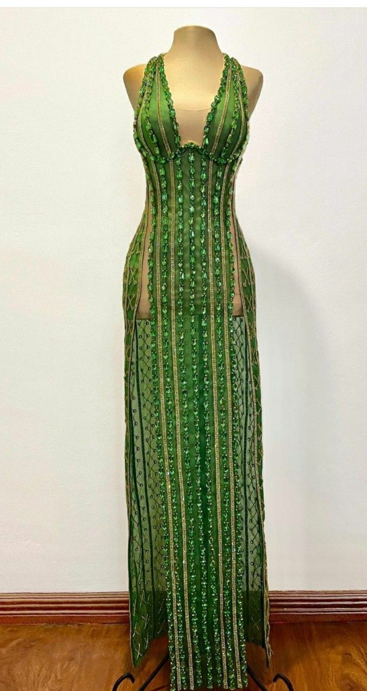 the image shows a sleeveless, green evening gown with intricate beadwork displayed on a mannequin. the gown has sheer panels on the sides, creating a slimming effect, and the front of the dress features vertical rows of beads. the top of the dress is a halter style with a deep vneckline, and the skirt is a floorlength design with slits at the sides. the beadwork appears to be a mix of green and gold, adding a touch of elegance to the dress.