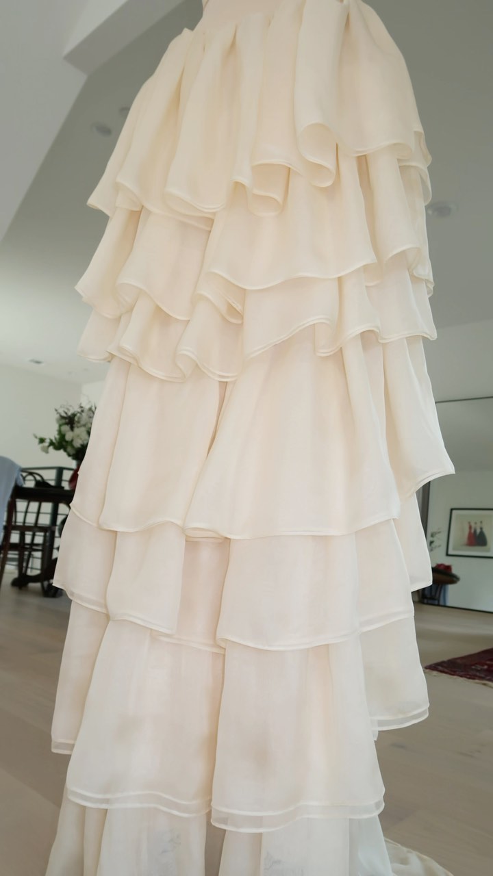 a white, ruffled skirt, possibly part of a wedding dress, hangs elegantly on a hanger. the skirt is tiered, with multiple layers of soft, flowing tulle creating a beautiful, ethereal look. the layers are intricately ruffled, adding a delicate and feminine touch. the skirt's white color and elegant design suggest a formal or special occasion, possibly a wedding.