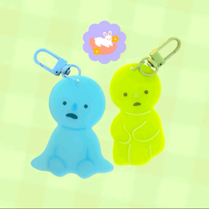 two cute jellylike keychains, one blue and one green. they are both shaped like people with silly expressions and are hanging from a ring. they are both cute and would make great gifts.
