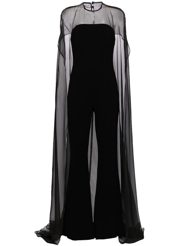 a woman wearing a black jumpsuit with a sheer cape. the jumpsuit is fitted and has a wide leg. the cape is long and flowing, and it is semitransparent. the woman is standing with her arms at her sides. the dress is a formal evening wear look.