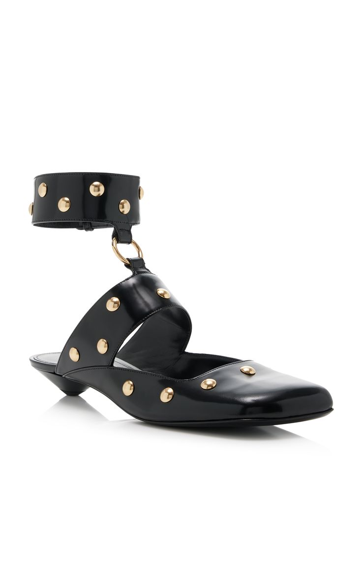 a pair of black leather mules with gold studs are shown against a white background.  the mules have an ankle strap with gold studs, and the shoe itself is also studded with gold embellishments. the shoes have a low heel.
