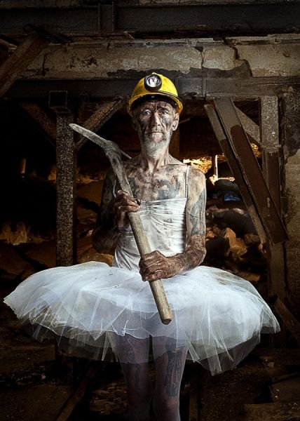 a man dressed as a ballerina stands in a dark, dilapidated mine shaft. he is wearing a white tutu, a hard hat, and a pickaxe. he is covered in coal dust and grime, and his expression is serious. the image is a surreal and thoughtprovoking juxtaposition of masculinity and femininity, labor and art, and the grit of the industrial world with the elegance of ballet.