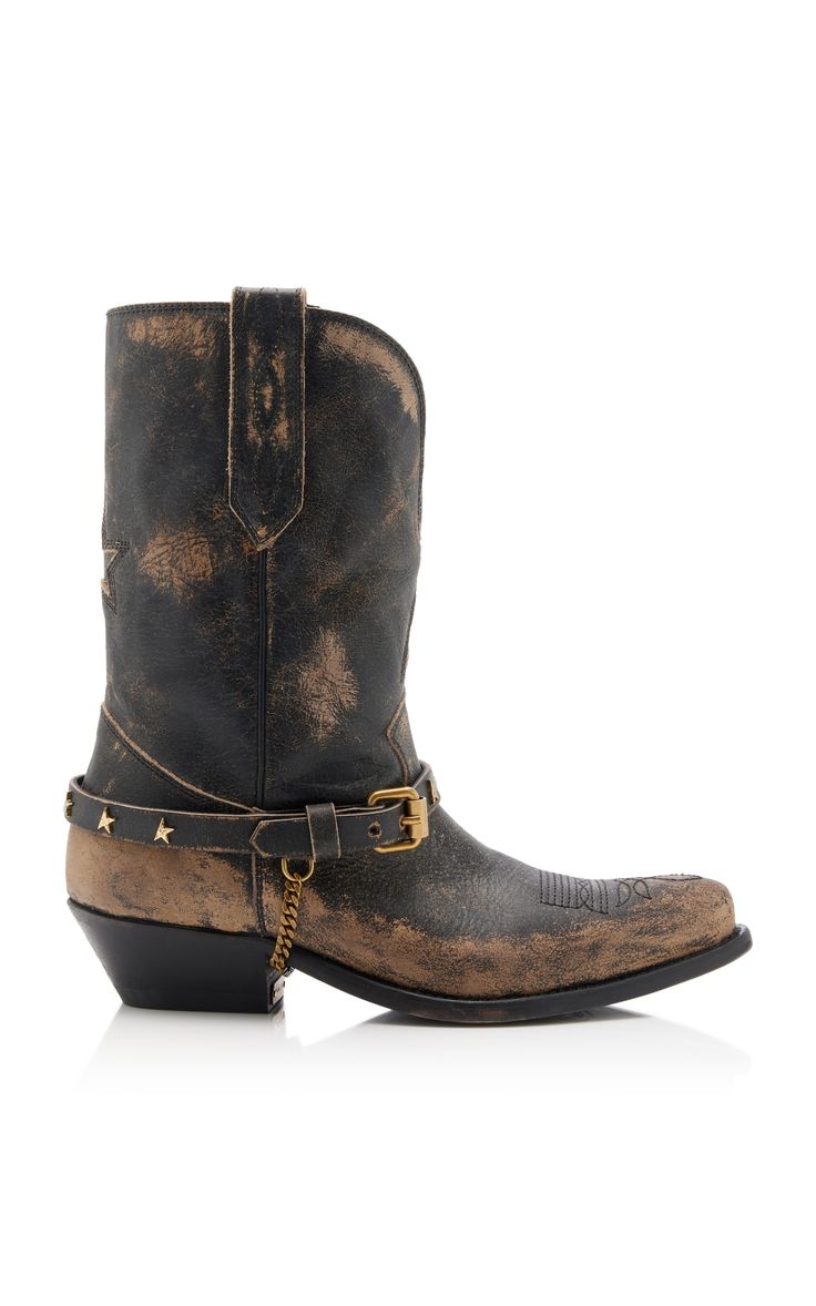 a studio shot of a pair of women's distressed black leather cowboy boots with gold hardware, including a buckle and chain detail. the boots have a midcalf height and feature a vintage or grunge style.  the leather appears worn and faded.  the background is white.