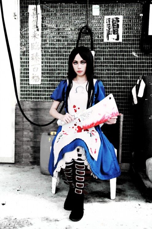 this image depicts a woman in a cosplay of the red queen from the novel alice in wonderland. she is dressed in a blue and white dress, complete with a bloody apron. she is holding a large, bloody cleaver in her hand.