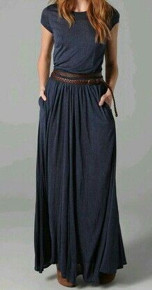 a young woman is wearing a long, blue maxi dress with a brown belt around her waist. she is standing in a casual pose, with her hair down and her arms at her sides. she is wearing a pair of brown sandals, and her overall look is stylish and elegant.