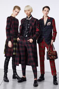 three women in stylish plaid outfits pose for a photo shoot. the woman in the middle is wearing a black and red plaid coat with black leggings, the woman on the left is wearing a black and red plaid skirt and black leggings, and the woman on the right is wearing a black and green plaid blazer with red plaid pants. all three women are wearing black boots and carrying black bags. they are standing against a white background.  they are looking chic and trendy.