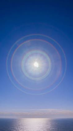 a vibrant blue sky with a bright sun, shining through clouds, creating a beautiful circular halo effect. the horizon meets the ocean, reflecting the sunlight in a shimmering glare. the scene is tranquil and peaceful, capturing the beauty of a clear summer day.