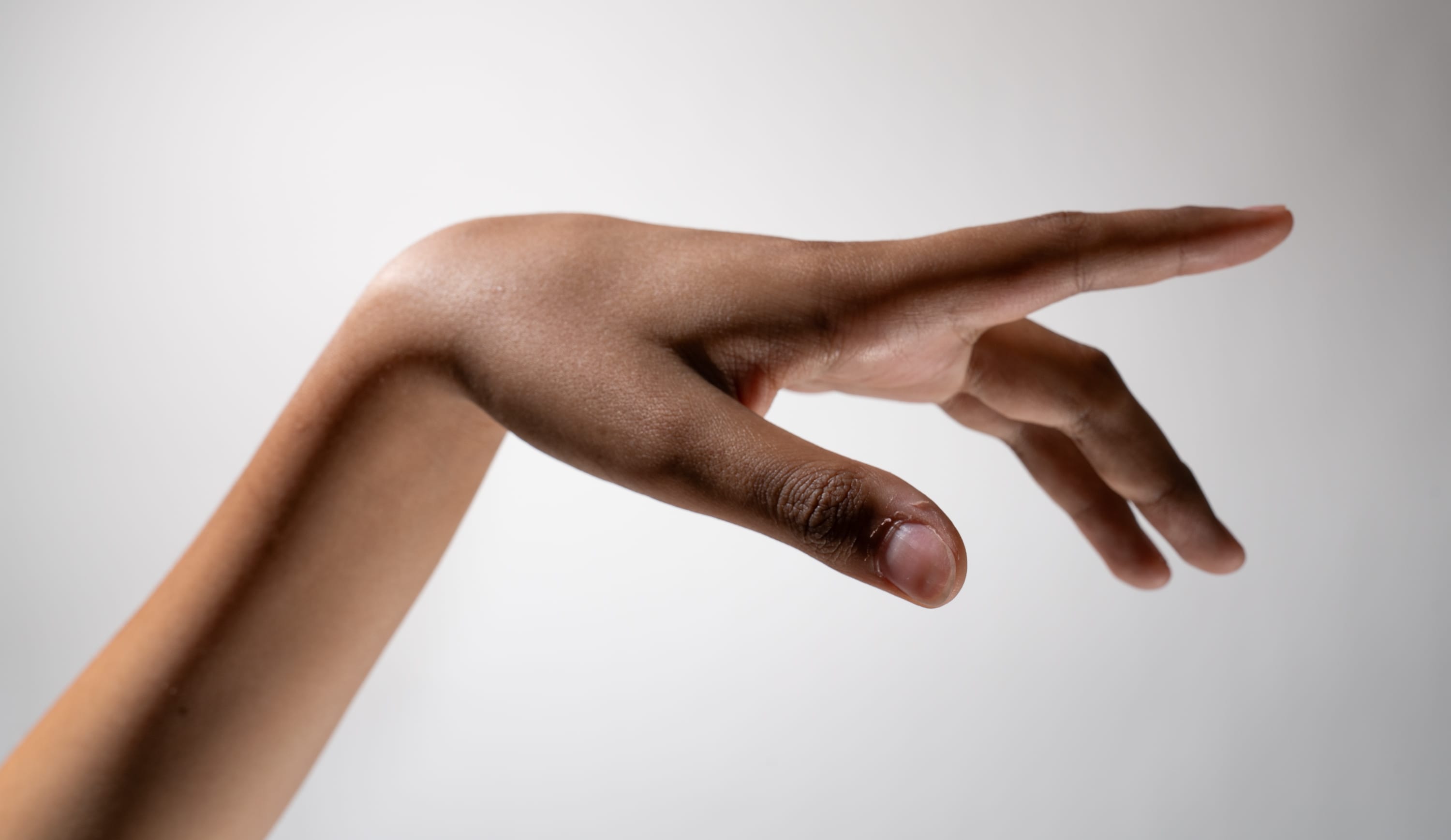 a closeup side view of a person's outstretched hand and arm against a light gray background. the hand is relaxed, with fingers slightly curled. the skin tone is medium brown, and the image highlights the natural texture of the skin.